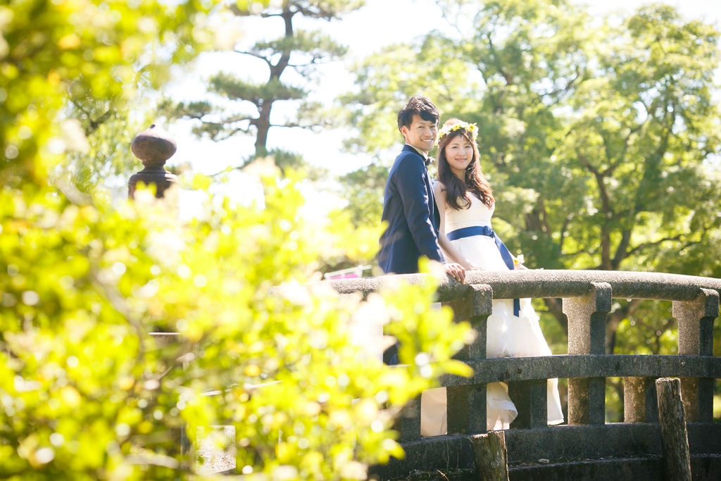 鶴舞公園の緑と橋の前でかわいい結婚写真を撮影中のふたり