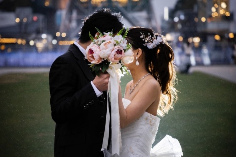 イルミネーションの前でブーケで隠しながら顔を寄せる新郎新婦