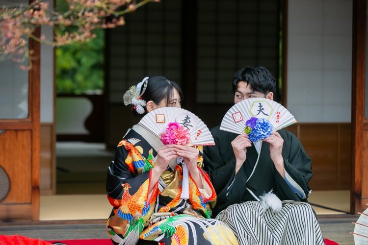 扇子で顔を隠しながら縁側に座る新郎新婦