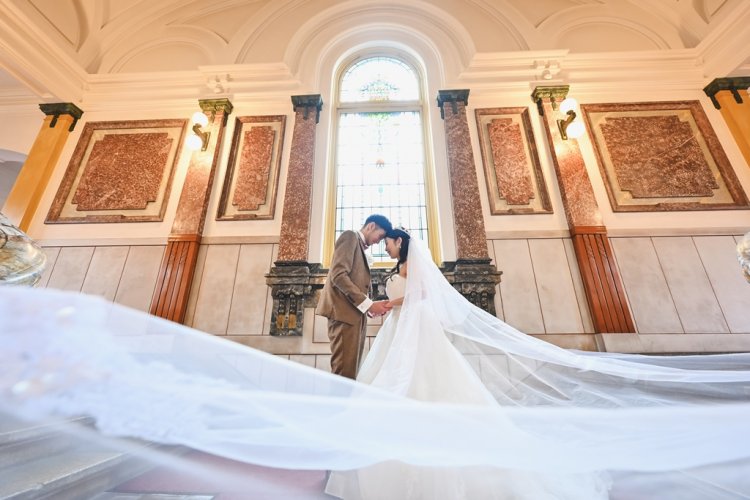 手をとりおでこを合わせヴェールをなびかせる新郎新婦