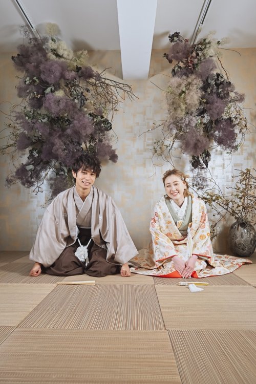 畳で二人並んで正座に三つ指ついて笑顔の新郎新婦