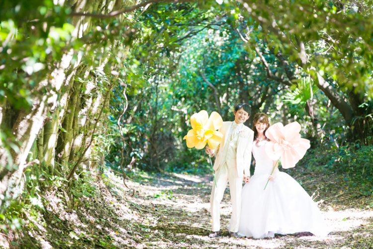 森の中で大きな花のオブジェを手に楽しそうな新郎新婦