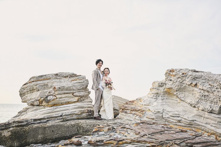 岩場で仲良く並んで海を眺める新郎新婦