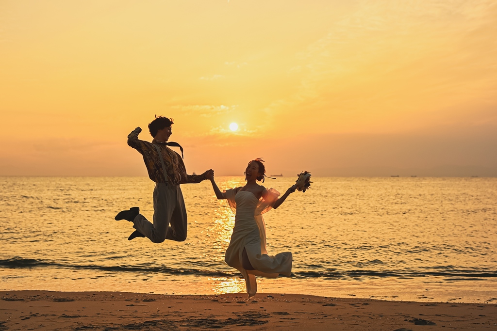 夕日バックに楽しそうに手をつないでジャンプする新郎新婦