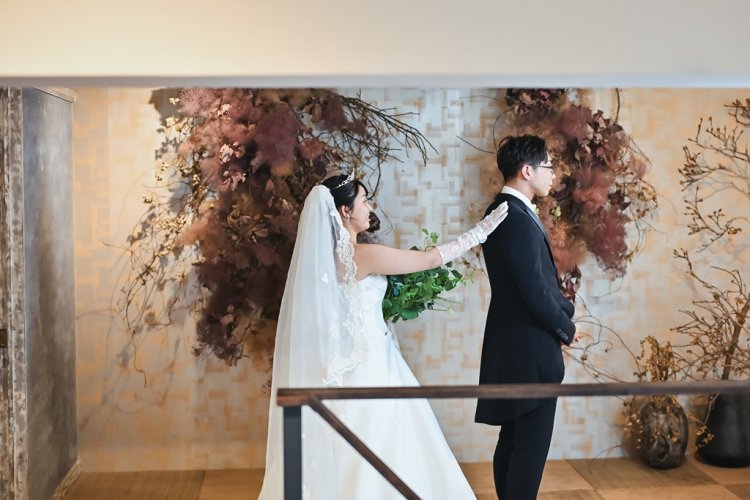 ドライフラワーオブジェ前で新郎の肩を後ろからそっとたたく新婦