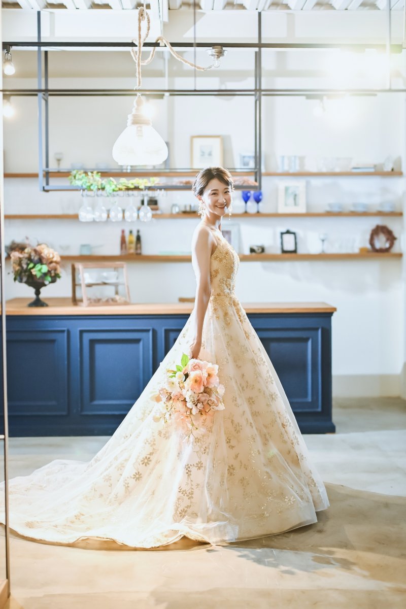 スタジオでブーケを持ちゴールドのドレスで微笑む新婦