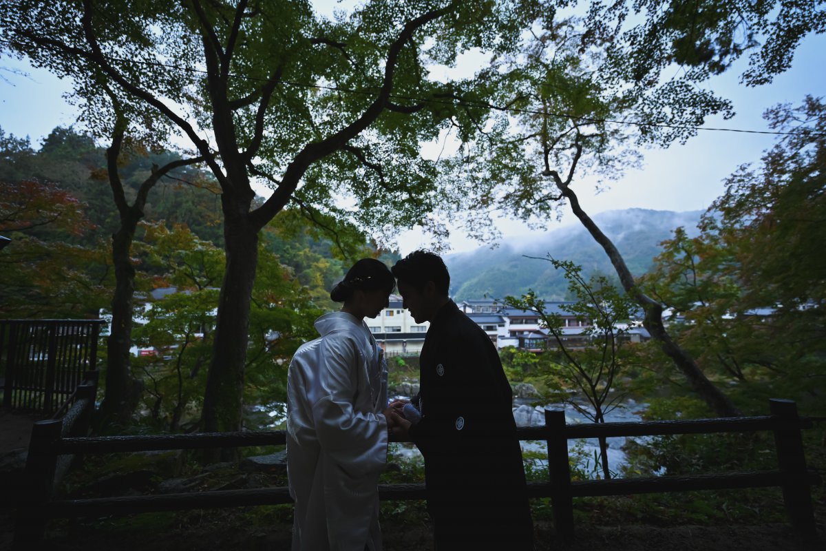 紅葉のトンネルの下を手を取り合って歩くポーズの新郎新婦