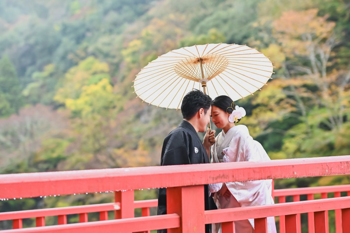 紅葉のトンネルの下を手を取り合って歩くポーズの新郎新婦
