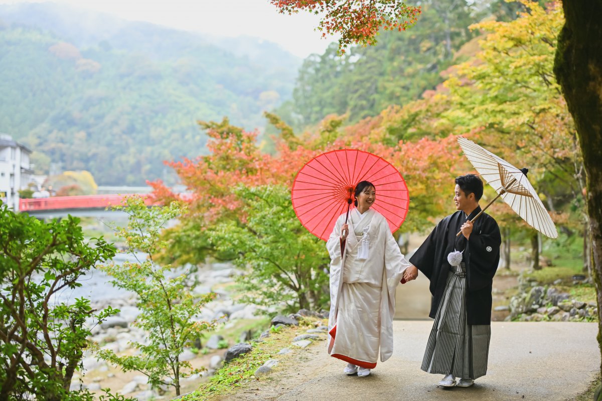 紅葉のトンネルの下を手を取り合って歩くポーズの新郎新婦