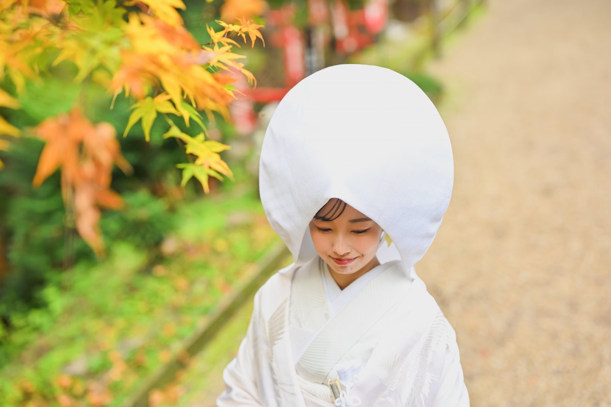 紅葉のトンネルの下を手を取り合って歩くポーズの新郎新婦