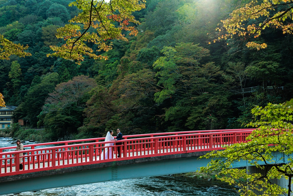 紅葉を背景に橋の上で寄り添い立つポーズの新郎新婦