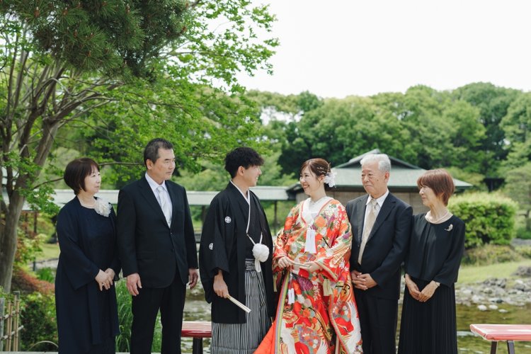 新緑の庭園で両家の親族と紋付袴の新郎、色打掛の新婦が並ぶ記念撮影、家族写真