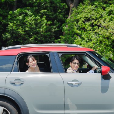 緑の木々を背に、赤いルーフの愛車に乗ってカメラに笑う新郎新婦。思い出の車で撮る前撮り
