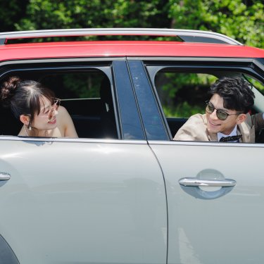 愛車の運転席と後部座席から顔を出し、見つめ合って笑う新郎新婦。車と一緒に撮るウェディングフォト