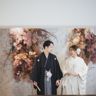 ピンクのドライフラワーの前に並んで立つ新郎新婦を、中二階から写した和装フォトウェディング