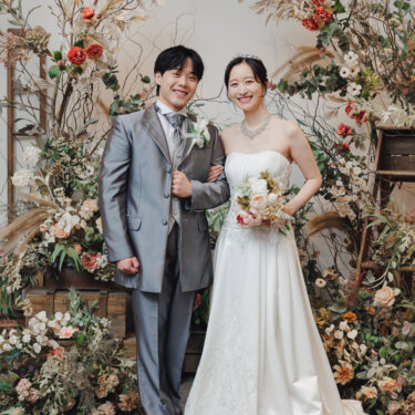 ドライフラワーの装飾と絨毯のセットで腕を組み、カメラに笑う新郎とウェディングドレスの花嫁のスタジオフォト