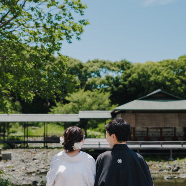 池と数寄屋の建物を眺めて赤い縁台に座る、白無垢の花嫁と紋付袴の新郎の後ろ姿の和装フォトウェディング