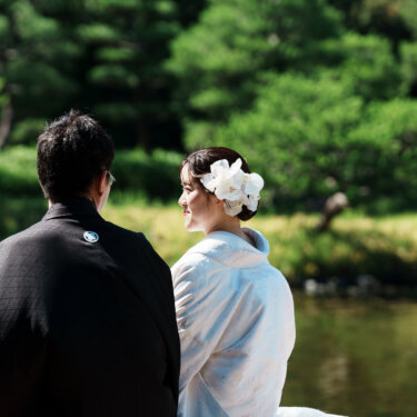 池を眺めて並ぶ新郎の後ろ姿と、振り返る白無垢の花嫁。白鳥庭園の緑が美しい和装前撮り