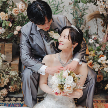 ドライフラワーに囲まれたセットで、振り返って新郎と見つめ合うティアラの花嫁のウェディングフォト