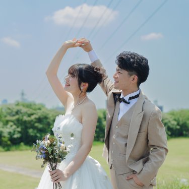 二人の腕でハートを作り、青空の下で寄り添う新郎新婦。河川敷で撮るかわいいポーズのウェディングフォト