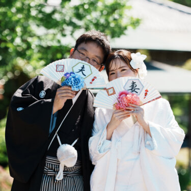 '夫''妻'と書かれた扇子で顔の下半分を隠し、目元で笑う新郎新婦。小物を使った和装前撮り