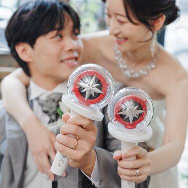 推しのペンライトを二人で掲げ、後ろから抱きつく花嫁と笑う新郎。好きなものを取り入れた遊び心ある前撮り