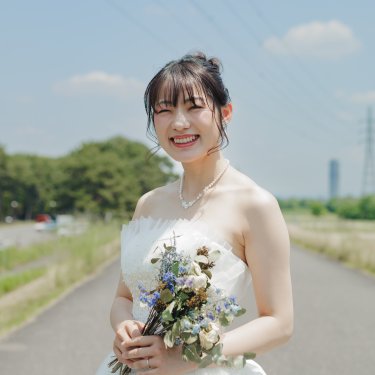 河川敷の道でブルー系のドライフラワーのブーケを持ち、笑顔を見せるウェディングドレスの花嫁。青空の下で撮る前撮り