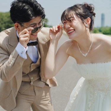 サングラスをずらして顔を寄せ、いたずらっぽく笑う新郎新婦。河川敷で撮る遊び心あるウェディングフォト