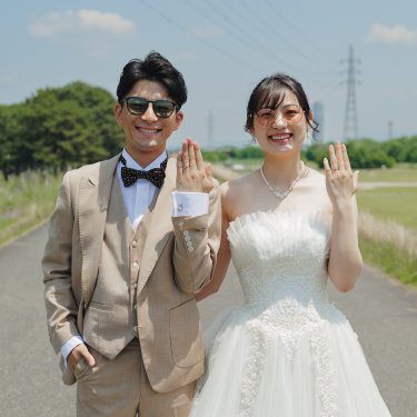河川敷の道で指輪をはめた手をカメラに向ける、サングラスの新郎新婦。結婚報告にも使える前撮り