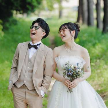 並木道で空を見上げて大笑いする、サングラスの新郎とウェディングドレスの花嫁の前撮り