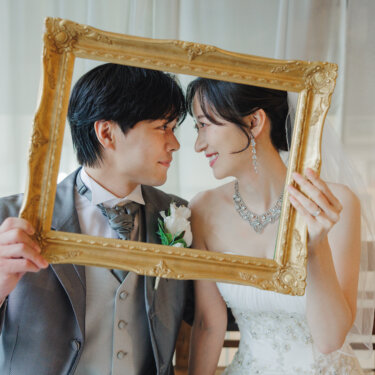金の額縁を二人で持ち、フレームの中で鼻先を寄せ合う新郎新婦。ウェディングドレスで撮る前撮り