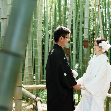 竹を前景にぼかし、竹林で手を取り見つめ合う紋付袴の新郎と白無垢の花嫁の和装フォトウェディング