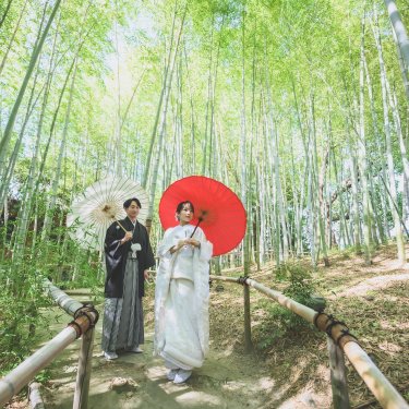 竹林の小道で白と赤の和傘を差して並ぶ新郎新婦を見上げるように写した、白鳥庭園の和装前撮り