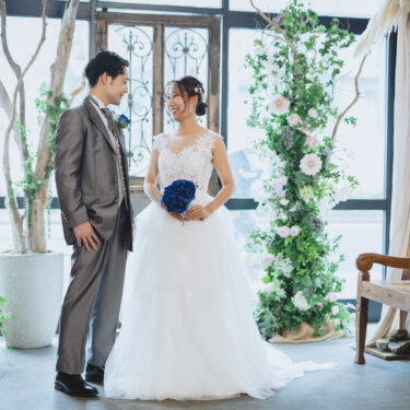 アンティークの扉と花のアーチのセットで向き合う、グレーのタキシードの新郎とウェディングドレスの花嫁の結婚写真