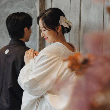 ドライフラワー越しに、新郎の胸に手を添えてほほえむ白無垢の花嫁。胡蝶蘭の髪飾りが映える和装フォトウェディング