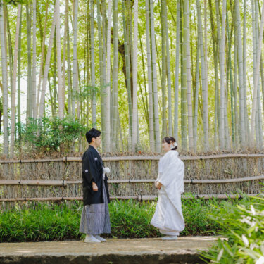 竹垣の前に広がる竹林で、少し離れて向き合う紋付袴の新郎と白無垢の花嫁を引きで写した和装前撮り