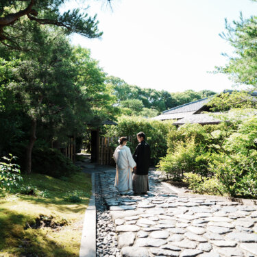 松と木々に囲まれた石畳の小道の奥に立つ新郎新婦。白鳥庭園の緑を大きく入れた和装ロケーションフォト