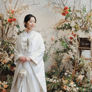 ドライフラワーのアーチの前でほほえむ白無垢の花嫁のソロショット。和装フォトウェディングの一枚
