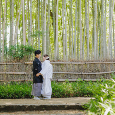 竹垣の前の竹林で、向き合って寄り添う新郎新婦を引きで写した緑豊かな和装フォトウェディング