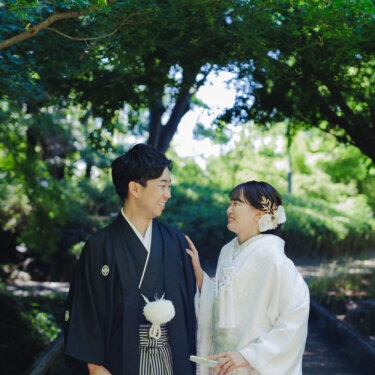 青もみじのトンネルの小道で、見つめ合って笑う紋付袴の新郎と白無垢の花嫁の和装前撮り