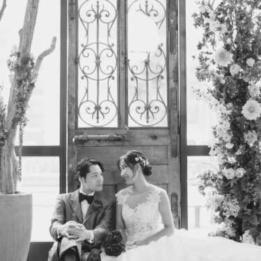 アイアン装飾の古い扉の前で床に座り、見つめ合う新郎新婦をモノクロで写した結婚写真