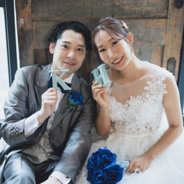 'K''H'のイニシャルのオブジェを顔の横に掲げて笑う新郎新婦。小物を使ったウェディングフォト