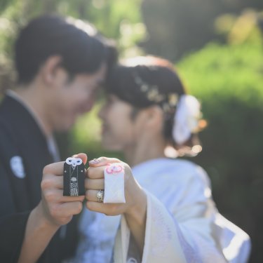'Mr''Mrs'のイニシャル小物を手に額を寄せ合う新郎新婦。前景をぼかした和装フォトウェディング