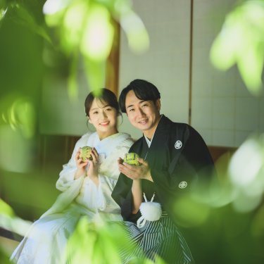 青もみじ越しに、縁側で抹茶の茶碗を持って笑う新郎新婦を写した和装フォトウェディング