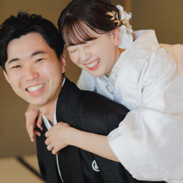 新郎の背中に抱きついて大笑いする白無垢の花嫁と、笑顔の新郎。仲の良さが伝わる和装フォトウェディング