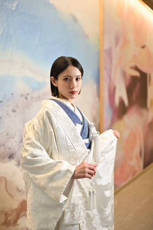 鶴を描いたアートウォールの前で、藍色の掛下に白無垢を重ねて佇む花嫁。スタジオでの和装前撮り